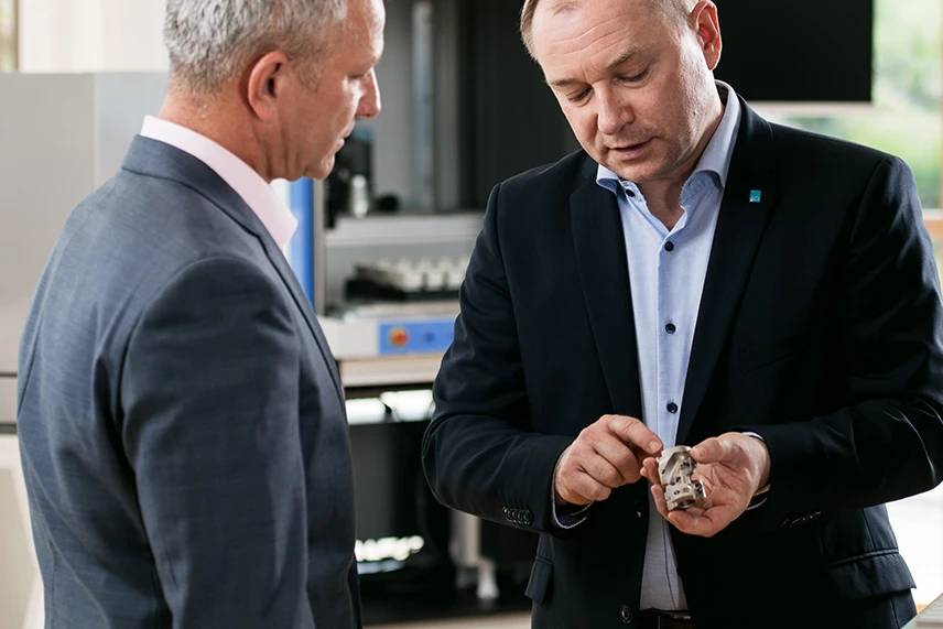 ACI Laser sales manager shows sample part in conversation with customers, showroom in the background