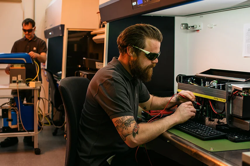 ACI Laser maintenance: employee with measuring device at the laser source, another employee at the fiber laser