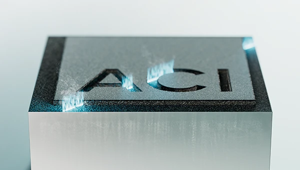 A metal workpiece with the ACI logo engraved on it and reflections of light.